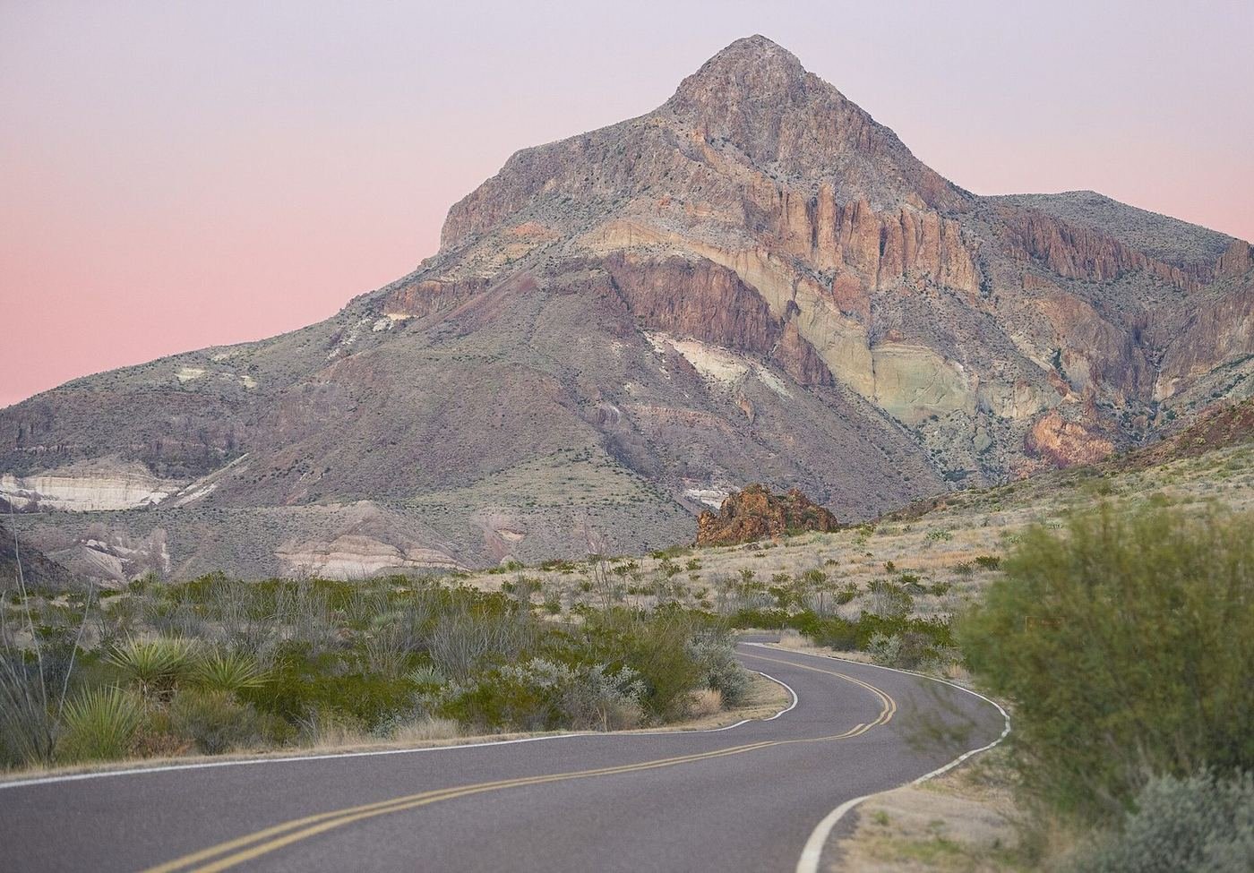 A winding road below a pink-sky sunset and a rugged desert peak in Big Bend National Park